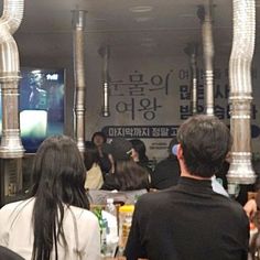 people are sitting at tables in front of a television screen with korean characters on it