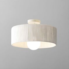 a white light hanging from the ceiling with a beige shade on it's side