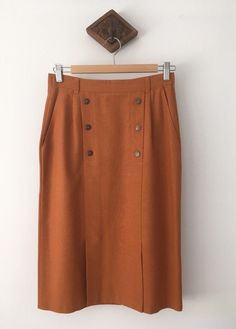 Don't go past this cute vintage rust coloured skirt from the 80s Features a very now rust colour,  *Decorative buttons,  *Zipper at the back with an elastic waist,  *A classic cut with a knee length finish *Is in perfect condition *has a 2 splits at the front  *pockets at the front  MEASUREMENTS: taken on a flat surface Length: 66cm or 26 inches  Waist: 33cm or 13 inches Hip: 37.5cm or 14.5 inches  Complete the look with a vintage tee and vintage leather slides in black   $13 Express shipping, a Vintage Brown Skirt With Buttons, Retro Brown Skirt With Button Closure, Vintage Midi Skirt, Rust Colour, Button Outfit, Brown Skirt, Orange Skirt, Button Skirt, Brown Skirts