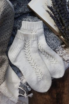 two pairs of socks and a book on a table next to lavender flowers, with an open book in the background