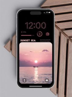 an iphone with the sunset sea on it's screen next to some wooden slats