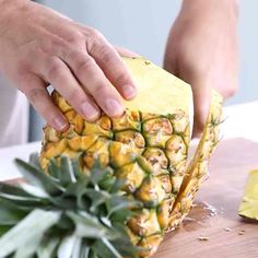 a person cutting up a pineapple on top of a wooden table