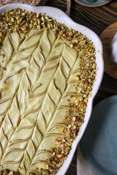 a pie with white frosting and nuts on top sitting in a dish next to plates