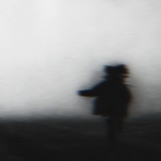 a blurry image of a person with a hat and coat walking in the fog