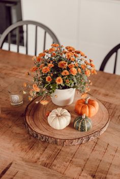 a wooden table topped with a white vase filled with orange flowers and mini pumpkins