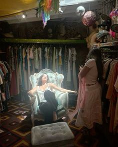 a woman sitting on a chair in a room full of clothes