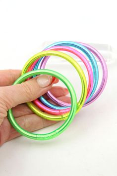 a hand holding a stack of multicolored bracelets on top of a white table