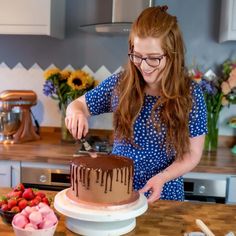 a woman cutting a chocolate cake on top of a wooden table