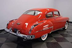 an old red car is parked on a checkered floor