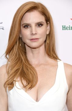 a woman with long red hair wearing a white dress and gold hoop earrings at an event