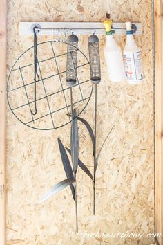 a metal bird feeder hanging from a wooden wall next to two bottles and a wire rack