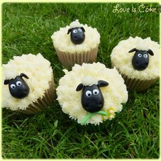 four cupcakes with fake sheep on them sitting in the middle of some grass