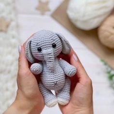 a person holding a small crocheted elephant in their left hand, next to some balls of yarn