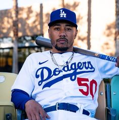 a baseball player sitting in the dugout with his bat on his shoulder and wearing a dodgers uniform