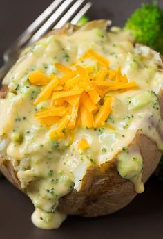 a baked potato covered in cheese and broccoli with a fork next to it