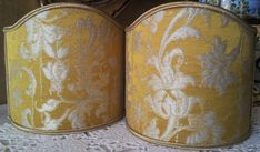 two yellow lampshades sitting on top of a white lace tablecloth covered table