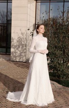 a woman in a white wedding dress standing on a brick walkway with her arms crossed