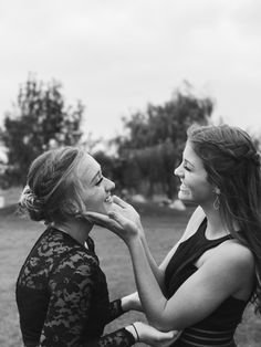 two women standing next to each other in a field with one touching the other's cheek