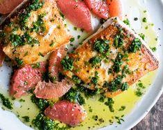 a white plate topped with fish covered in sauce and garnished with green herbs