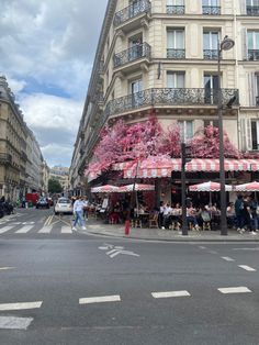 people are sitting at tables in the middle of an empty street with pink flowers on trees