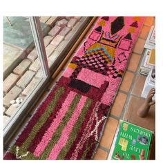 a pink and green rug sitting on top of a tiled floor next to a window