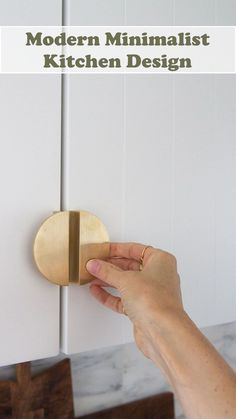 a hand is holding the door knob to a cabinet with white cabinets in the background