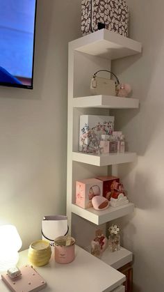 a white shelf filled with lots of items on top of a table next to a flat screen tv