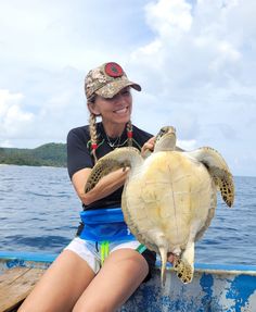 a woman sitting on the back of a boat holding a turtle