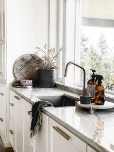 a kitchen with white cabinets and marble counter tops is pictured in this image, there are plants on the window sill next to the sink