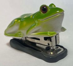 a green frog figurine sitting on top of a stapler with red eyes