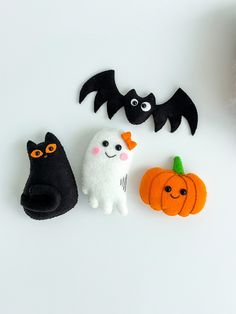 three felt halloween decorations on a white surface with pumpkins, ghost, and black cat