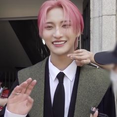 a young man with pink hair wearing a suit and tie, standing next to other people