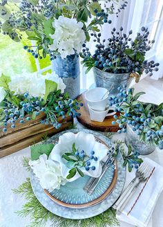 a table set with blue and white flowers in vases, plates and utensils