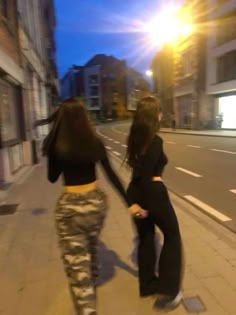 two young women walking down the street holding hands and looking at something in the distance