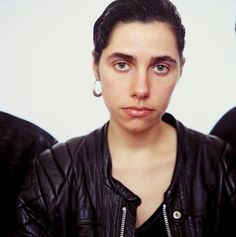 a woman wearing a black leather jacket and silver hoop earrings is looking at the camera