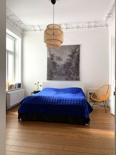 a bedroom with a blue bed and wooden floors in front of a painting on the wall