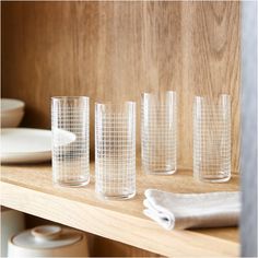 four glasses are lined up on a shelf in front of plates and napkins, one is empty