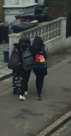 two girls walking down the street with backpacks on their back and one girl holding onto another