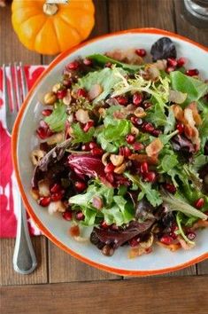 a salad with nuts and greens in an orange rimmed bowl on a wooden table