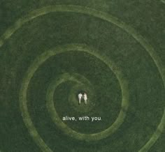 two people standing in the middle of a green field with an inscription above them that says alive with you