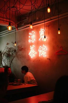 two people sitting at a table in a restaurant with neon lights hanging from the ceiling