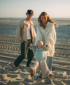 a man and woman are walking on the beach with a small child in their arms