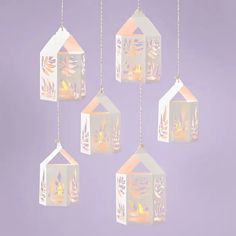 four paper lanterns hanging from chains on a purple background with leaves and plants in them