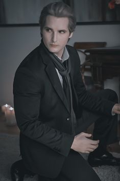 a man in a suit and tie sitting on the floor next to a table with candles