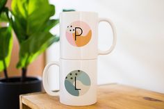 two coffee mugs sitting on top of a wooden table next to a potted plant