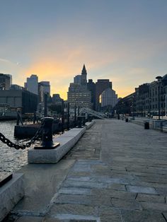 the sun is setting over the water in front of some buildings and a chain link fence