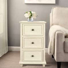 a white chair sitting in front of a painting on the wall next to a table with flowers