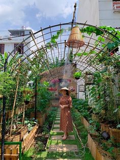 a woman in a brown dress and straw hat walking down a path through a garden