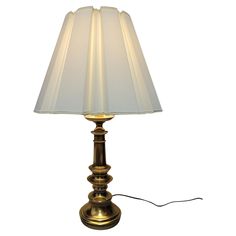 a gold lamp with a white shade on it's side and a cord attached to the base