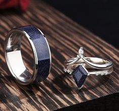 two wedding rings with blue and white diamonds on them sitting on a wooden table next to each other